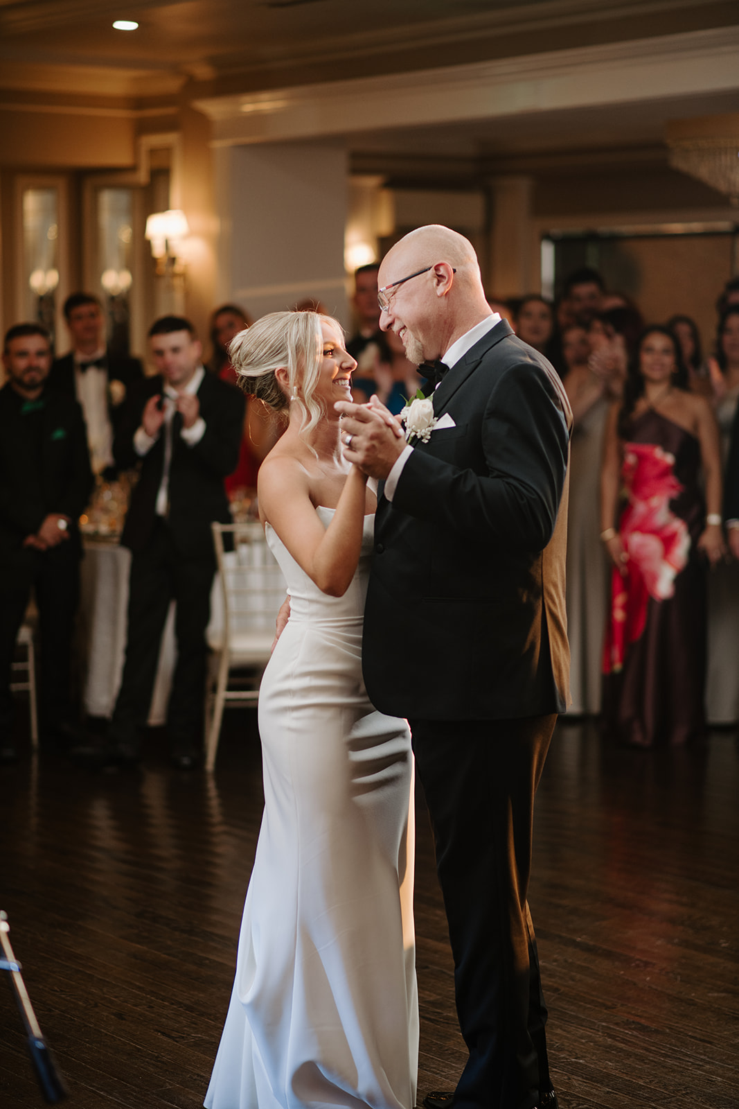 Bride shares a heartwarming father-daughter dance, smiling warmly under the reception lights.